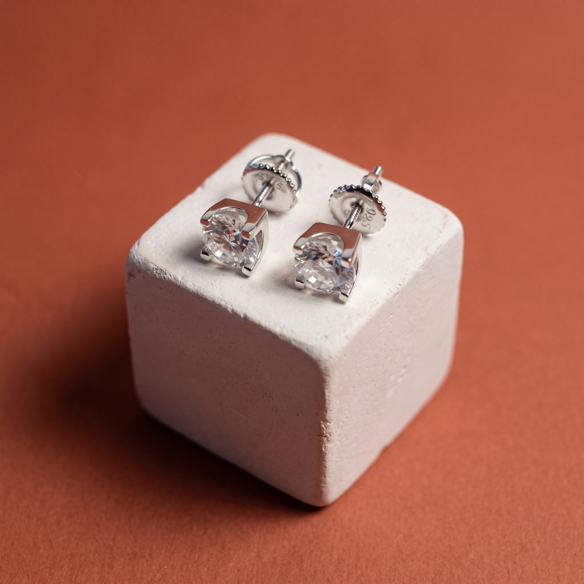 Moissanite solitaire studs on a plaster cube against terracotta