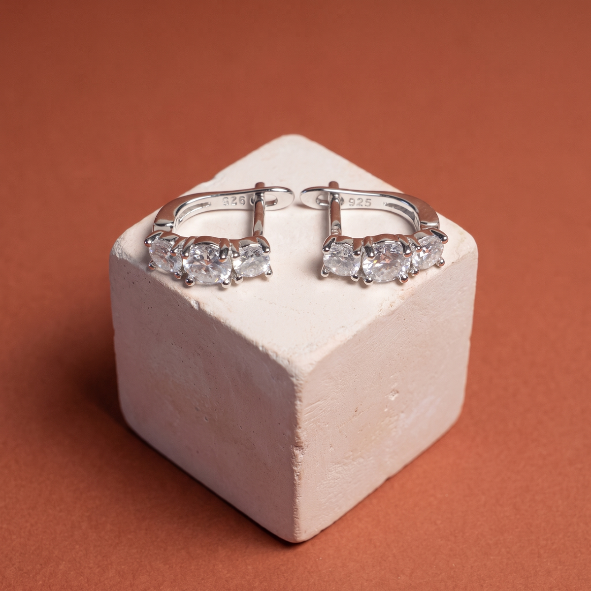Three-stone moissanite lever-backs on a plaster cube against terracotta