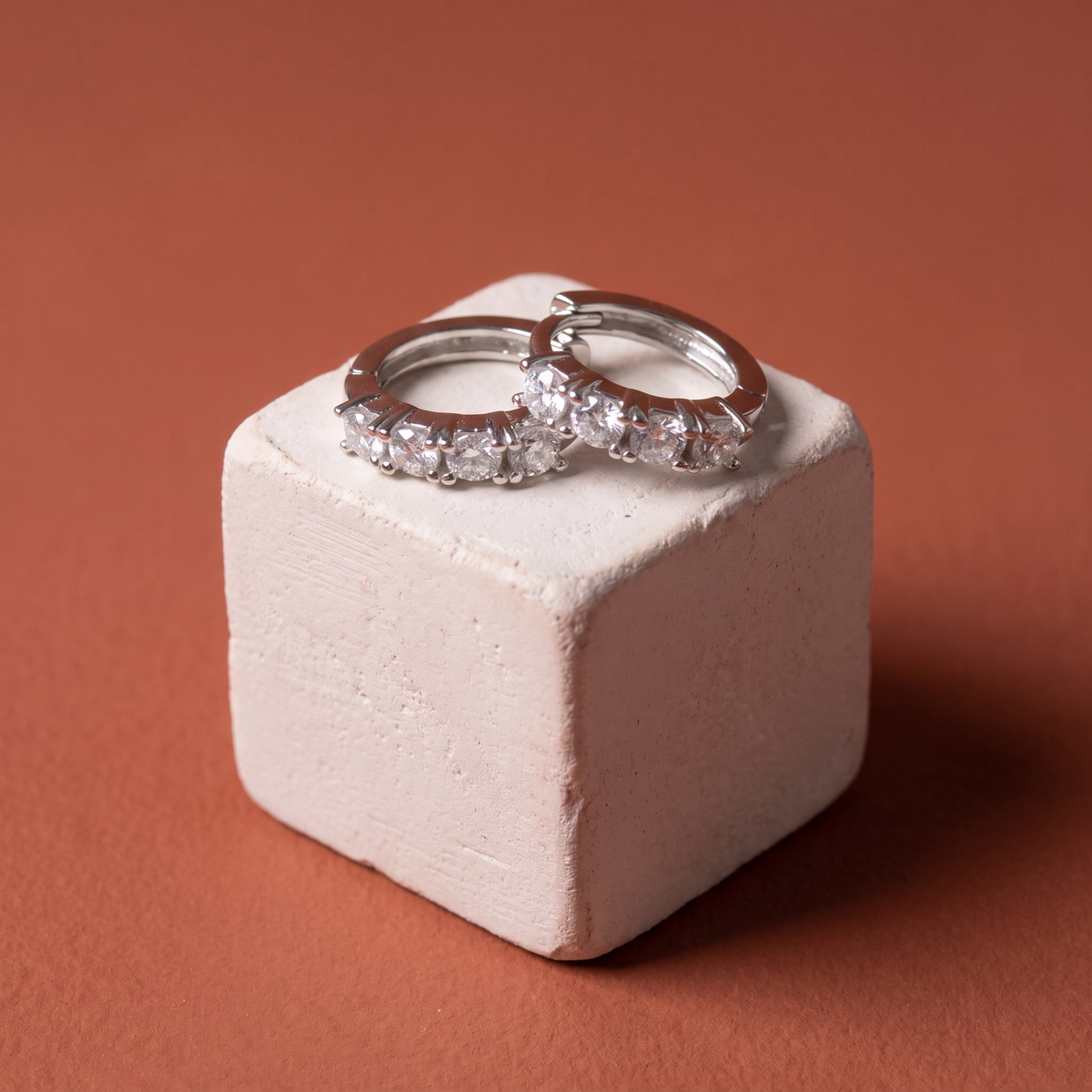 Four-stone moissanite huggies on a plaster cube against terracotta