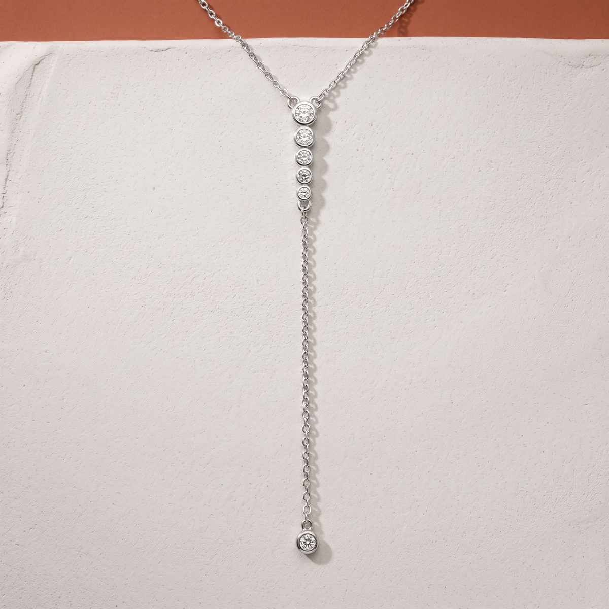 Moissanite lariat necklace on a plaster slab against terracotta